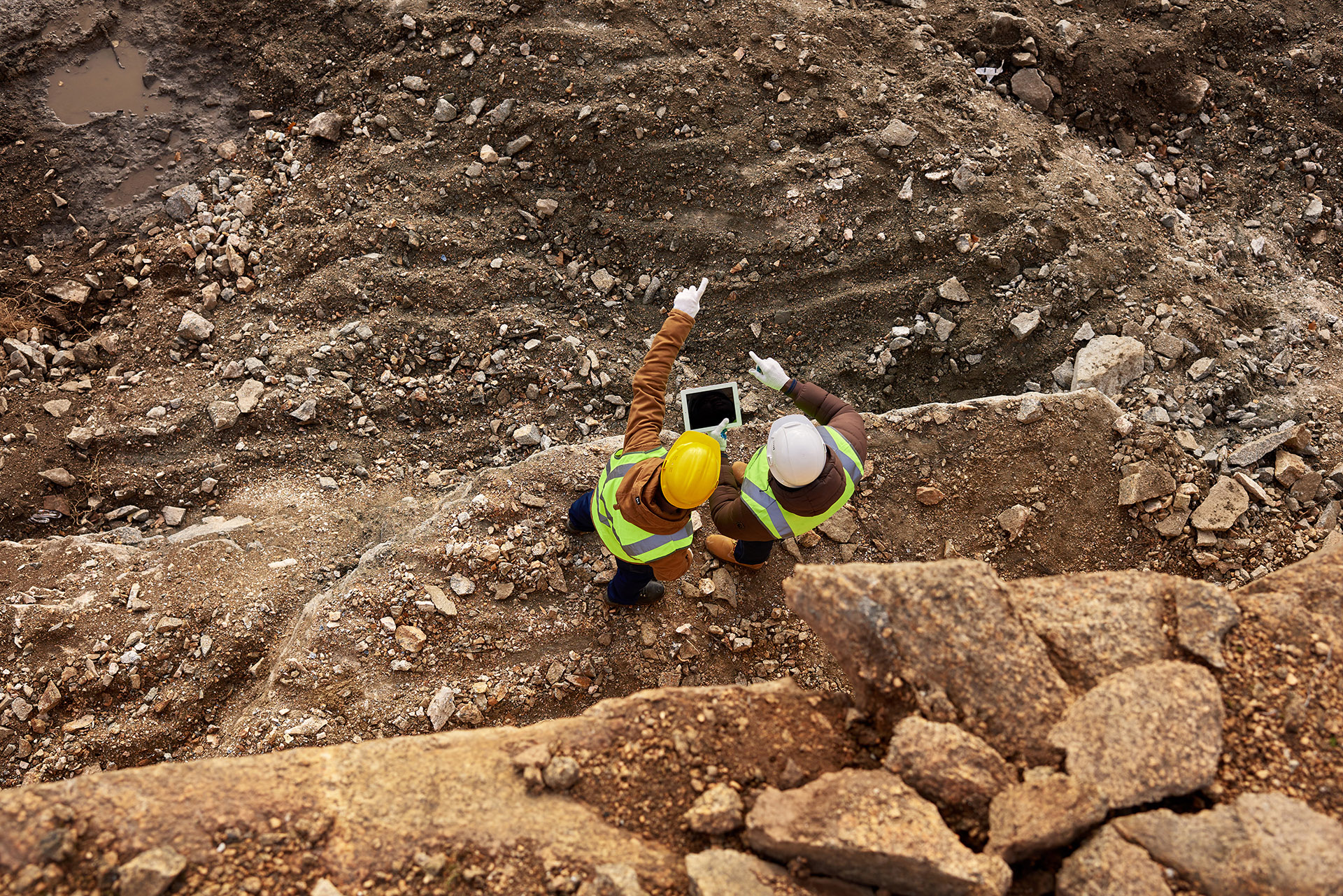 Top view shot of two industrial workers wearing reflective jackets standing on mining worksite outdoors using digital tablet, copy space